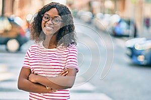 Young african american girl with arms crossed smiling happy standing at the city