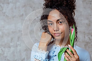A young African american girl in a blue dress with a Tulip on a gray background. Women`s day concept