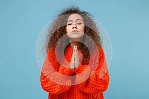 Young african american girl in casual orange knitted clothes hands folded in prayer isolated on pastel blue background