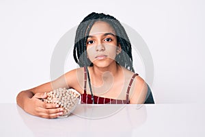 Young african american girl child with braids holding chickpeas bowl thinking attitude and sober expression looking self confident