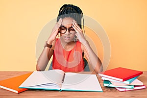 Young african american girl child with braids studying for school exam suffering from headache desperate and stressed because pain