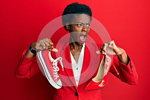 Young african american girl choosing high heel shoes and sneakers angry and mad screaming frustrated and furious, shouting with