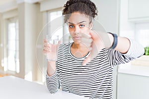 Young african american girl drinking a fresh glass of water with angry face, negative sign showing dislike with thumbs down,