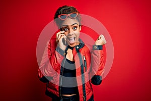 Young african american girl having conversation talking on the smartphone over red background screaming proud and celebrating