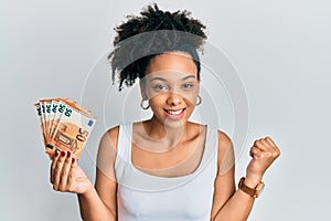 Young african american girl holding 50 euro banknotes screaming proud, celebrating victory and success very excited with raised