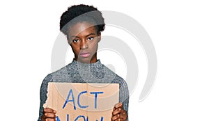 Young african american girl holding act now banner thinking attitude and sober expression looking self confident