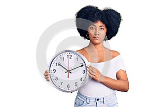 Young african american girl holding big clock thinking attitude and sober expression looking self confident