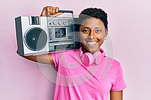 Young african american girl holding boombox, listening to music looking positive and happy standing and smiling with a confident