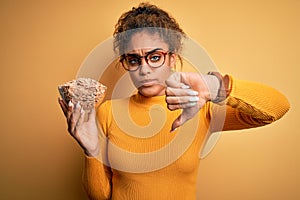 Young african american girl holding bowl with healthy cornflakes cereals over yellow background with angry face, negative sign