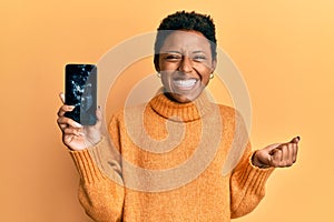 Young african american girl holding broken smartphone showing cracked screen screaming proud, celebrating victory and success very