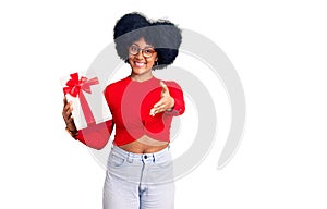 Young african american girl holding gift smiling friendly offering handshake as greeting and welcoming