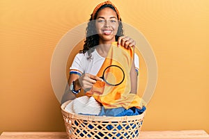 Young african american girl holding magnifying glass looking for stain at clothes smiling with a happy and cool smile on face