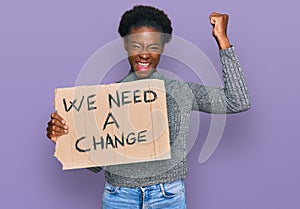 Young african american girl holding we need a change banner screaming proud, celebrating victory and success very excited with