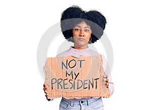 Young african american girl holding not my president protest banner thinking attitude and sober expression looking self confident