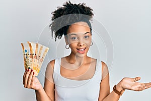 Young african american girl holding philippine peso banknotes celebrating achievement with happy smile and winner expression with