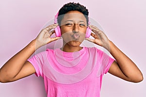 Young african american girl listening to music using headphones looking at the camera blowing a kiss being lovely and sexy