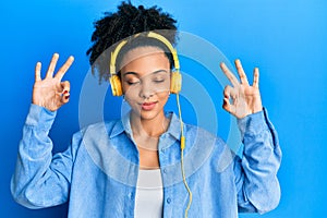 Young african american girl listening to music using headphones relax and smiling with eyes closed doing meditation gesture with