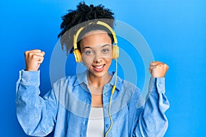 Young african american girl listening to music using headphones screaming proud, celebrating victory and success very excited with