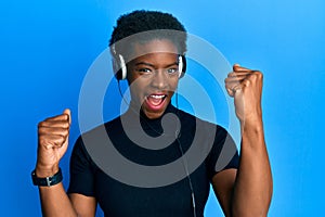 Young african american girl listening to music using headphones screaming proud, celebrating victory and success very excited with