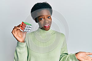 Young african american girl playing colorful puzzle cube intelligence game celebrating achievement with happy smile and winner