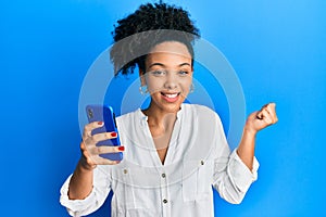 Young african american girl using smartphone screaming proud, celebrating victory and success very excited with raised arm