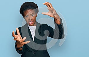 Young african american girl wearing business clothes shouting frustrated with rage, hands trying to strangle, yelling mad