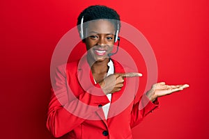 Young african american girl wearing call center agent headset amazed and smiling to the camera while presenting with hand and