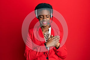 Young african american girl wearing call center agent headset smiling with hands on chest with closed eyes and grateful gesture on