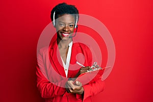 Young african american girl wearing call center agent headset writing on clipboard smiling with a happy and cool smile on face