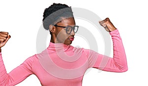 Young african american girl wearing casual clothes and glasses showing arms muscles smiling proud