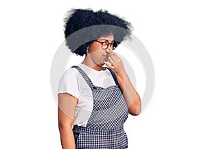 Young african american girl wearing casual clothes smelling something stinky and disgusting, intolerable smell, holding breath