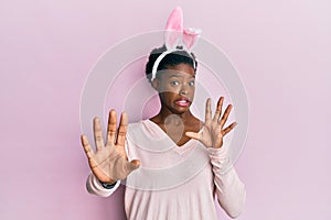 Young african american girl wearing cute easter bunny ears afraid and terrified with fear expression stop gesture with hands,