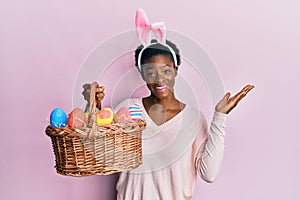 Young african american girl wearing cute easter bunny ears holding basket with painted eggs celebrating victory with happy smile