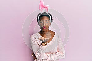 Young african american girl wearing cute easter bunny ears looking at the camera blowing a kiss with hand on air being lovely and