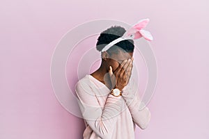 Young african american girl wearing cute easter bunny ears with sad expression covering face with hands while crying