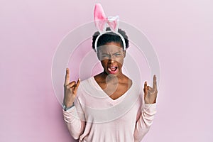 Young african american girl wearing cute easter bunny ears shouting with crazy expression doing rock symbol with hands up