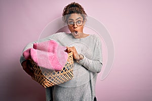 Young african american girl wearing glasses doing housework holding wicker basket with clothes scared in shock with a surprise