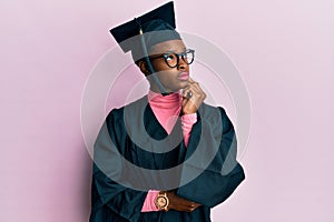 Young african american girl wearing graduation cap and ceremony robe with hand on chin thinking about question, pensive expression