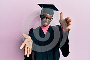 Young african american girl wearing graduation cap and ceremony robe looking at the camera smiling with open arms for hug