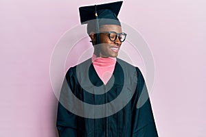 Young african american girl wearing graduation cap and ceremony robe smiling looking to the side and staring away thinking