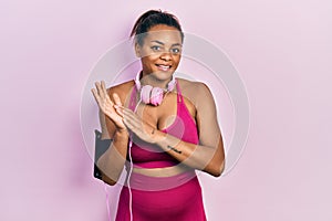 Young african american girl wearing gym clothes and using headphones clapping and applauding happy and joyful, smiling proud hands