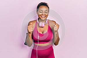 Young african american girl wearing gym clothes and using headphones excited for success with arms raised and eyes closed