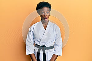 Young african american girl wearing karate kimono and black belt afraid and shocked with surprise expression, fear and excited