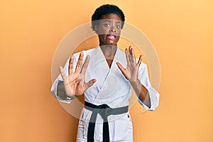 Young african american girl wearing karate kimono and black belt afraid and terrified with fear expression stop gesture with