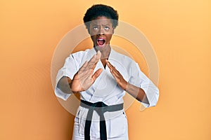 Young african american girl wearing karate kimono and black belt angry and mad screaming frustrated and furious, shouting with