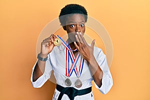 Young african american girl wearing karate kimono and black belt covering mouth with hand, shocked and afraid for mistake
