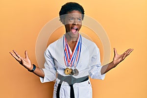 Young african american girl wearing karate kimono and black belt crazy and mad shouting and yelling with aggressive expression and