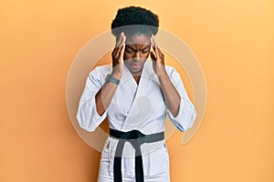 Young african american girl wearing karate kimono and black belt with hand on head for pain in head because stress