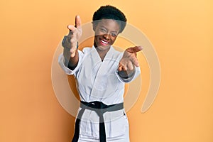 Young african american girl wearing karate kimono and black belt looking at the camera smiling with open arms for hug