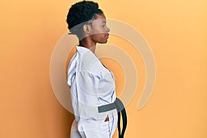 Young african american girl wearing karate kimono and black belt looking to side, relax profile pose with natural face with